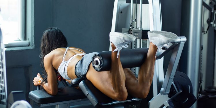 mujer hace leg curl en maquina