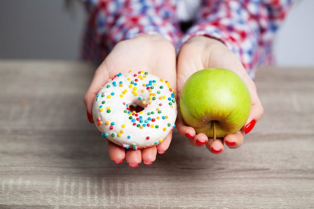 una persona eligiendo entre una dona y una manzana